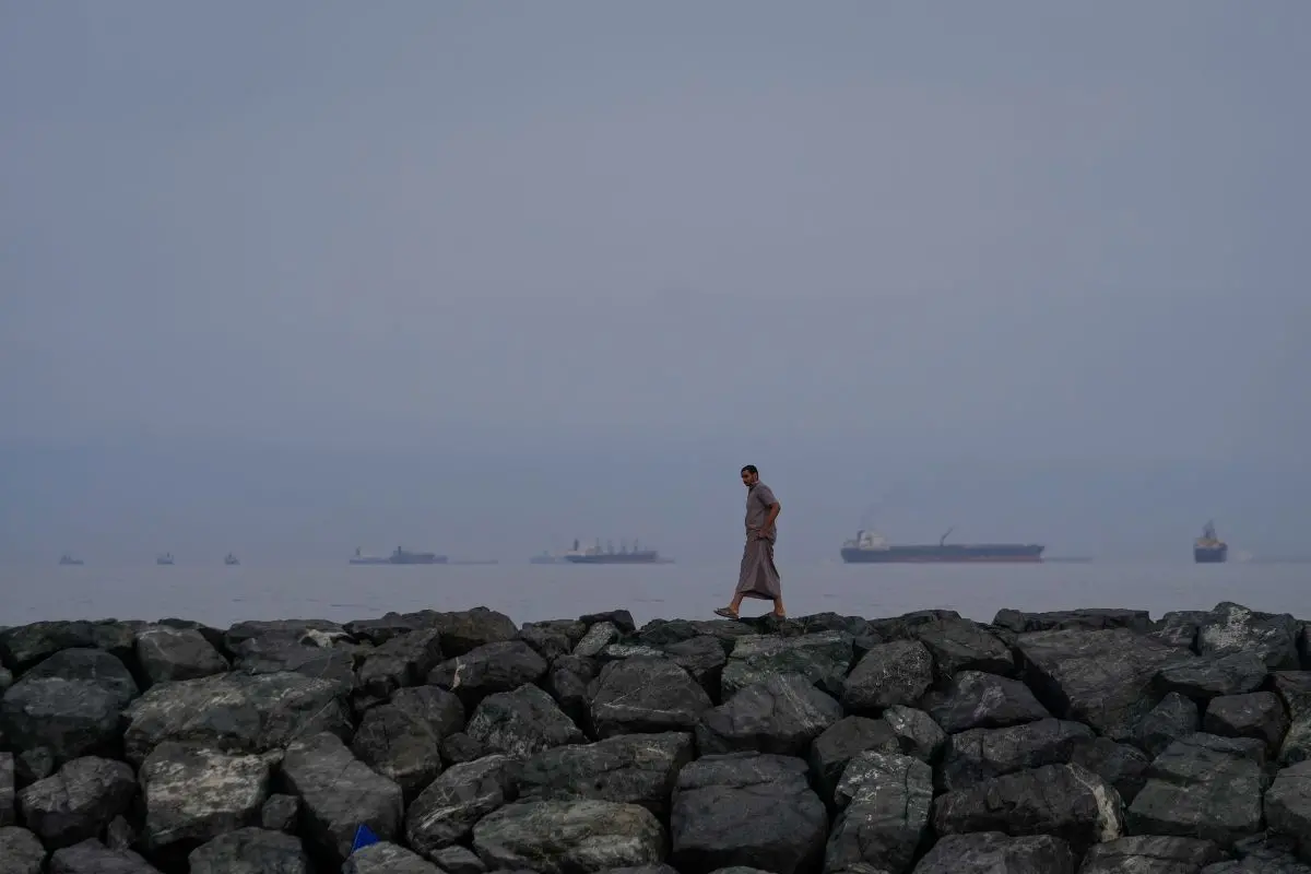 A man walks along the shore as oil tankers and cargo ships line up in the Strait of Hormuz (Photo: AP)