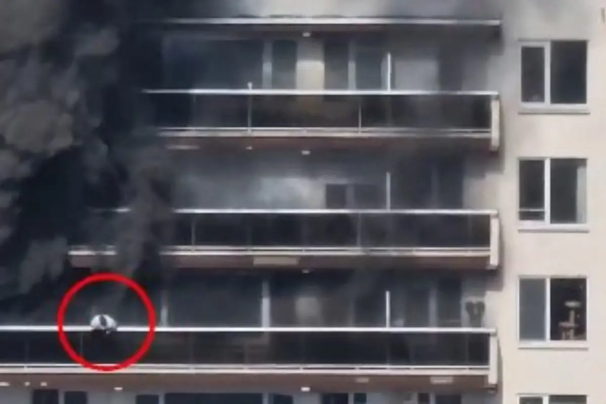 Thick black smoke billows from a high-rise apartment building in Antwerp, Belgium, as a resident is seen on a balcony during the deadly fire. The red circle highlights the person visible amid the smoke.
