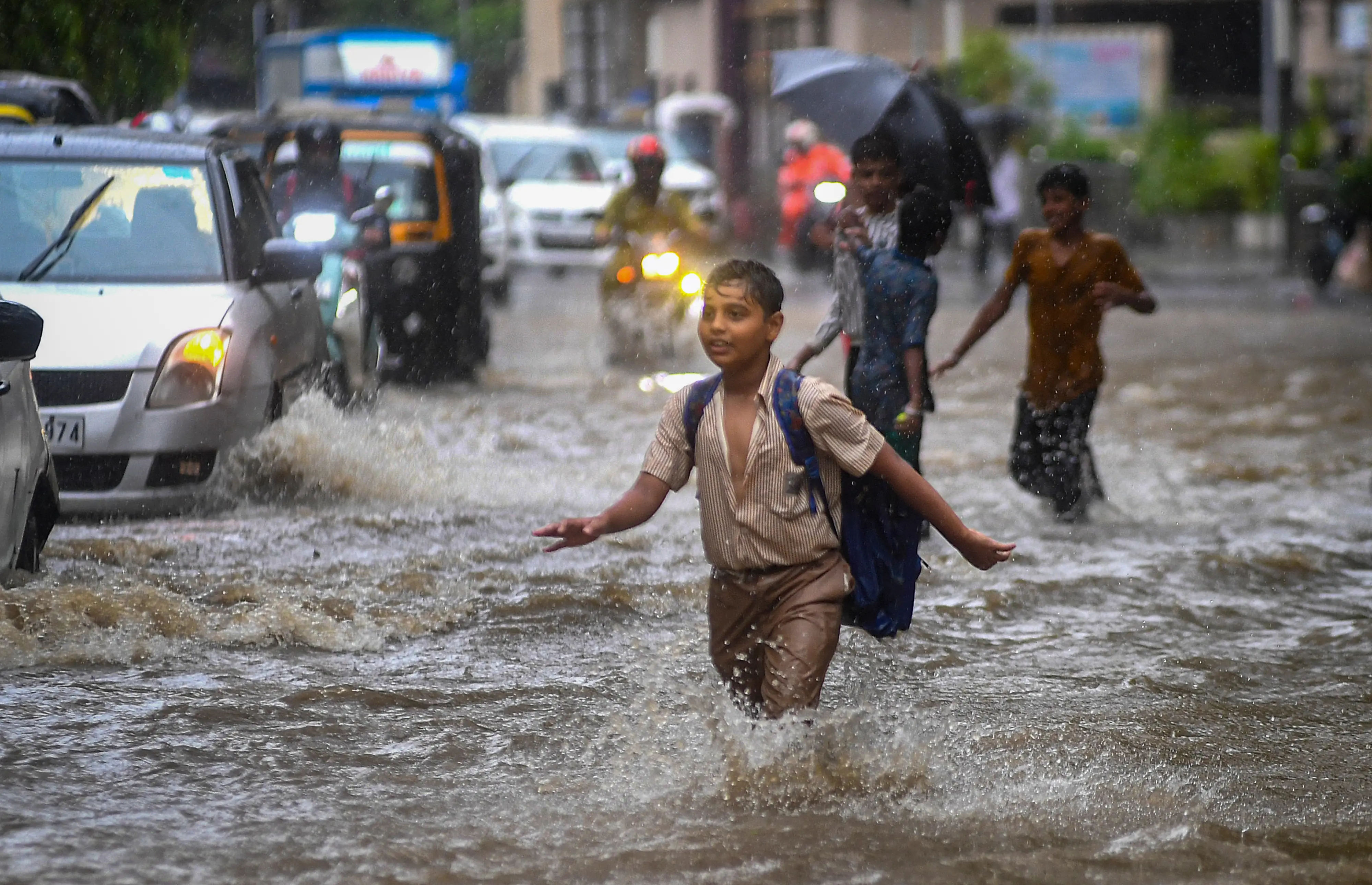 Children wade through a waterlogged area as vehicles pass by during rain, at Andheri area, in Mumbai, Maharashtra.| Photo: PTI