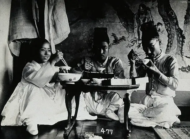 Koreans eating a meal, seated behind a small table, in front of a painted screen, circa 1900 | Image: Heritage Art