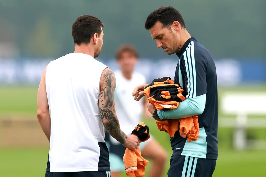 Lionel Scaloni, Head Coach of Argentina, hands in bibs to Lionel Messi of Argentina during a training session