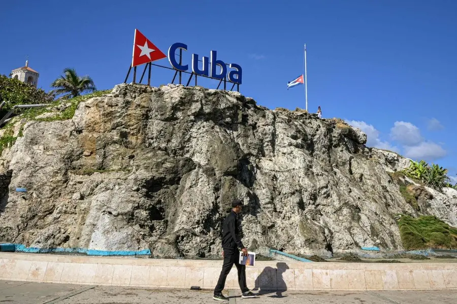 A Cuban man walks by a Cuba sign and national flag at half-mast in Havana on January 5, 2026. Havana declared two days of national mourning as of January 5 after a total of 32 Cubans were killed during the US attack on Caracas that culminated in the capture of Venezuela's president Nicolas Maduro.