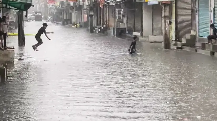 Children enjoy in a submerged market street following rainfall at the Sangam Vihar area, in New Delhi on Thursday | ANI