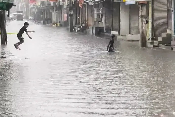 Children enjoy in a submerged market street following rainfall at the Sangam Vihar area, in New Delhi on Thursday