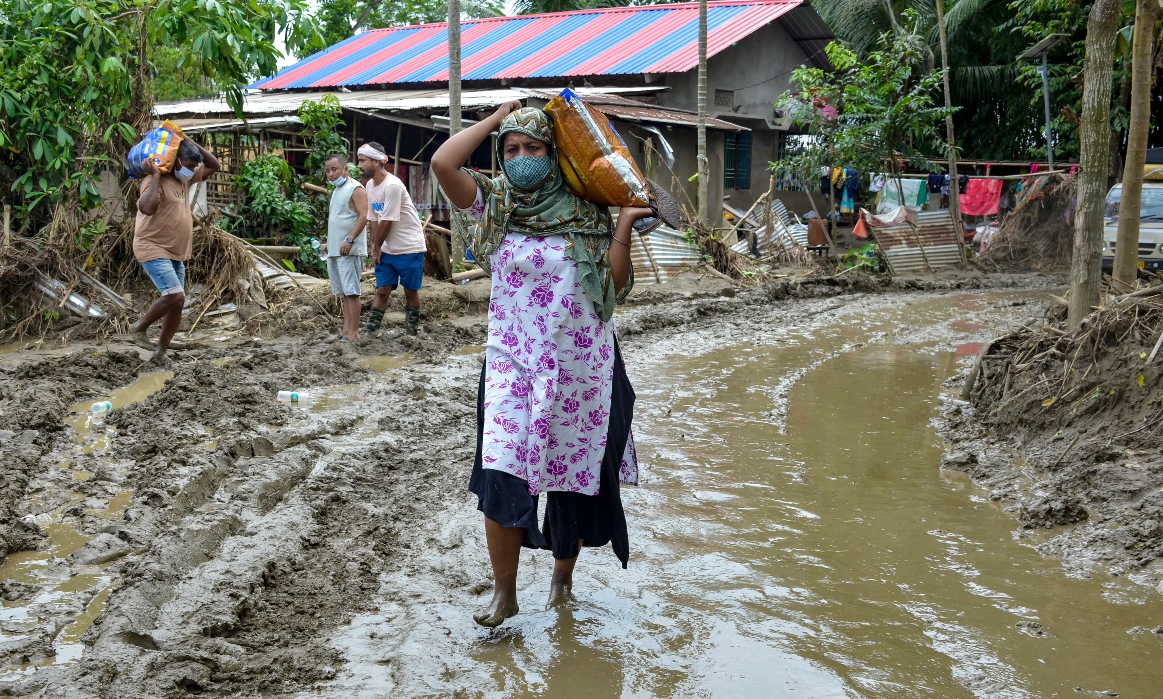 A flood-affected woman carries relief supplies through a muddy road in Sivasagar district, Assam | Photo: PTI