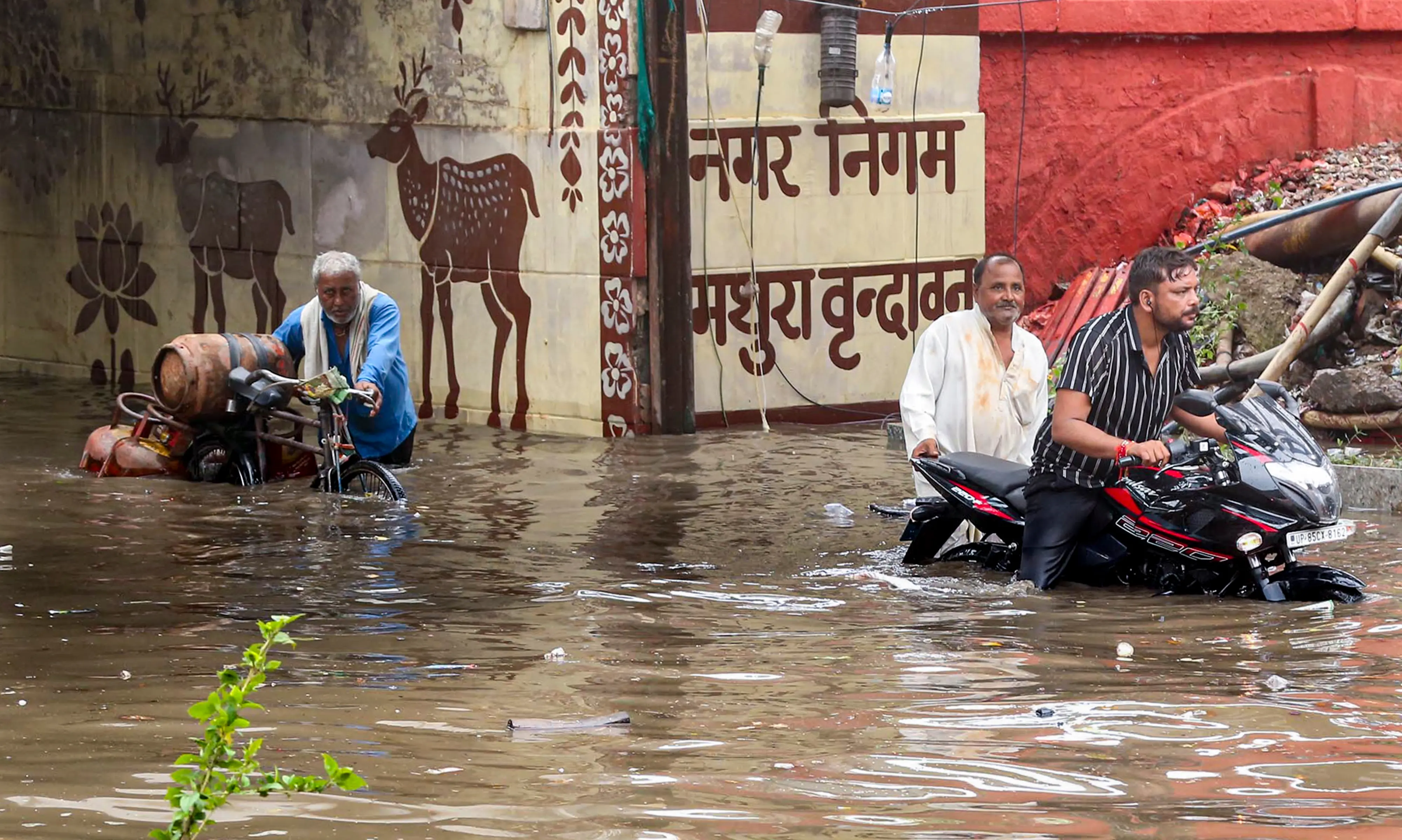 Commuters wade through a waterlogged road following rainfall, in Mathura, Uttar Pradesh | Photo: PTI