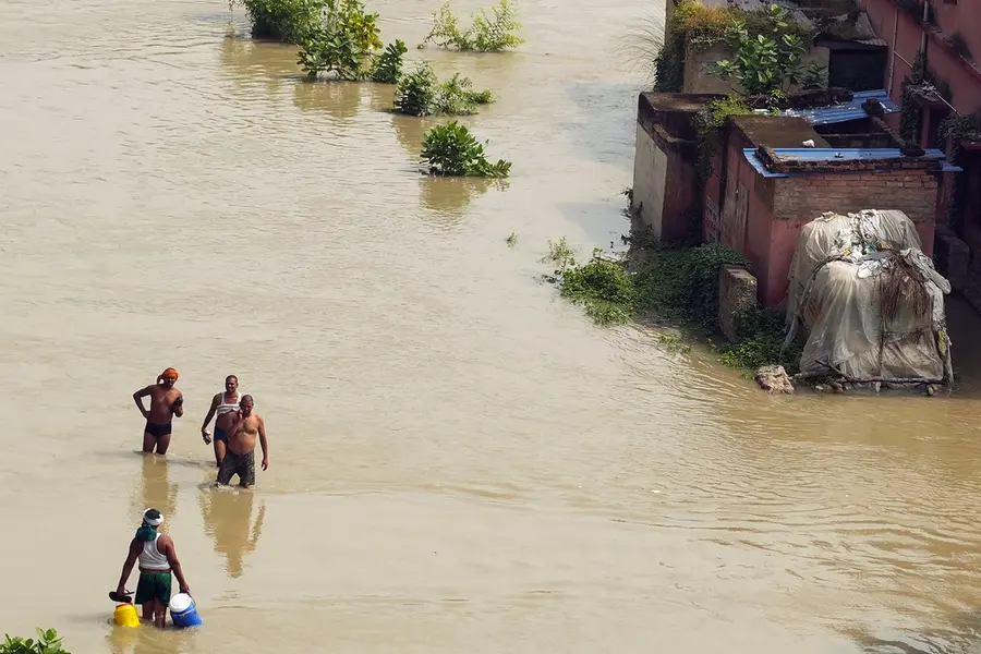 People wade through an inundated area following the rising water level of the Ganga River in Vaishali