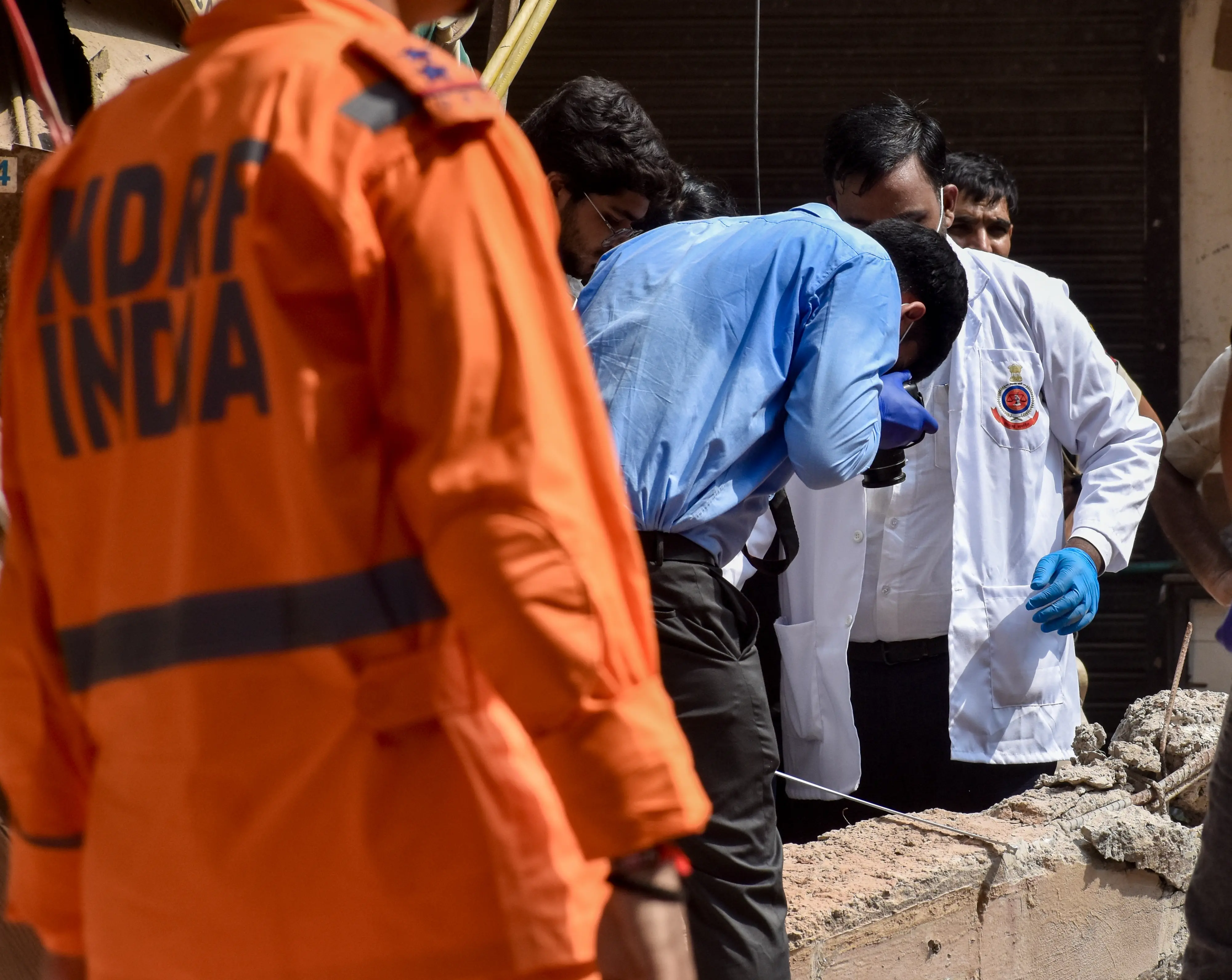 Forensic team members inspect the debris during search and rescue operations, a day after a five-storey building housing a boys' hostel collapsed, at Satya Niketan, in New Delhi.| Photo: PTI