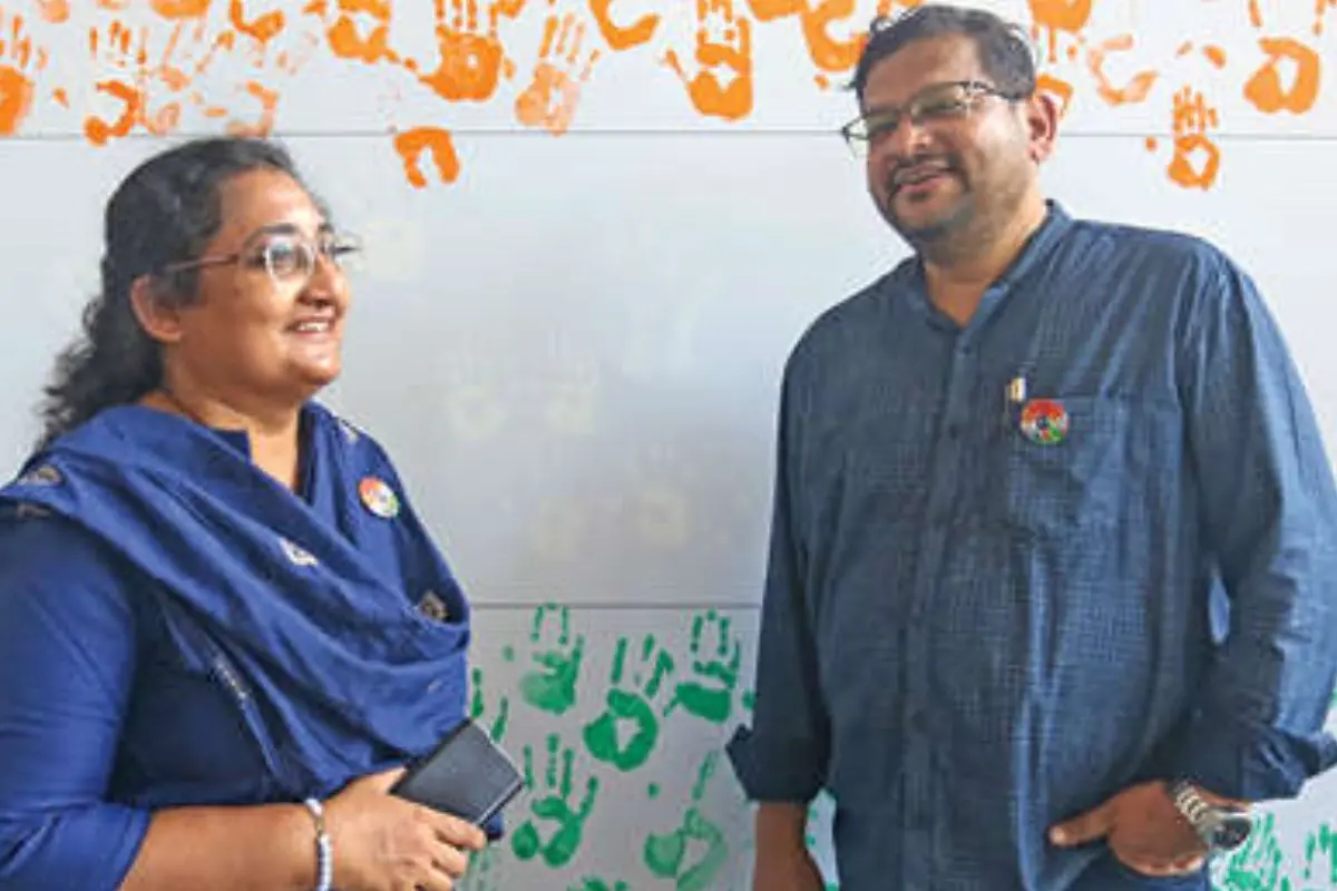 Sunil Baby and Liji Sunil in front of a canvas featuring handprints of specially-abled children