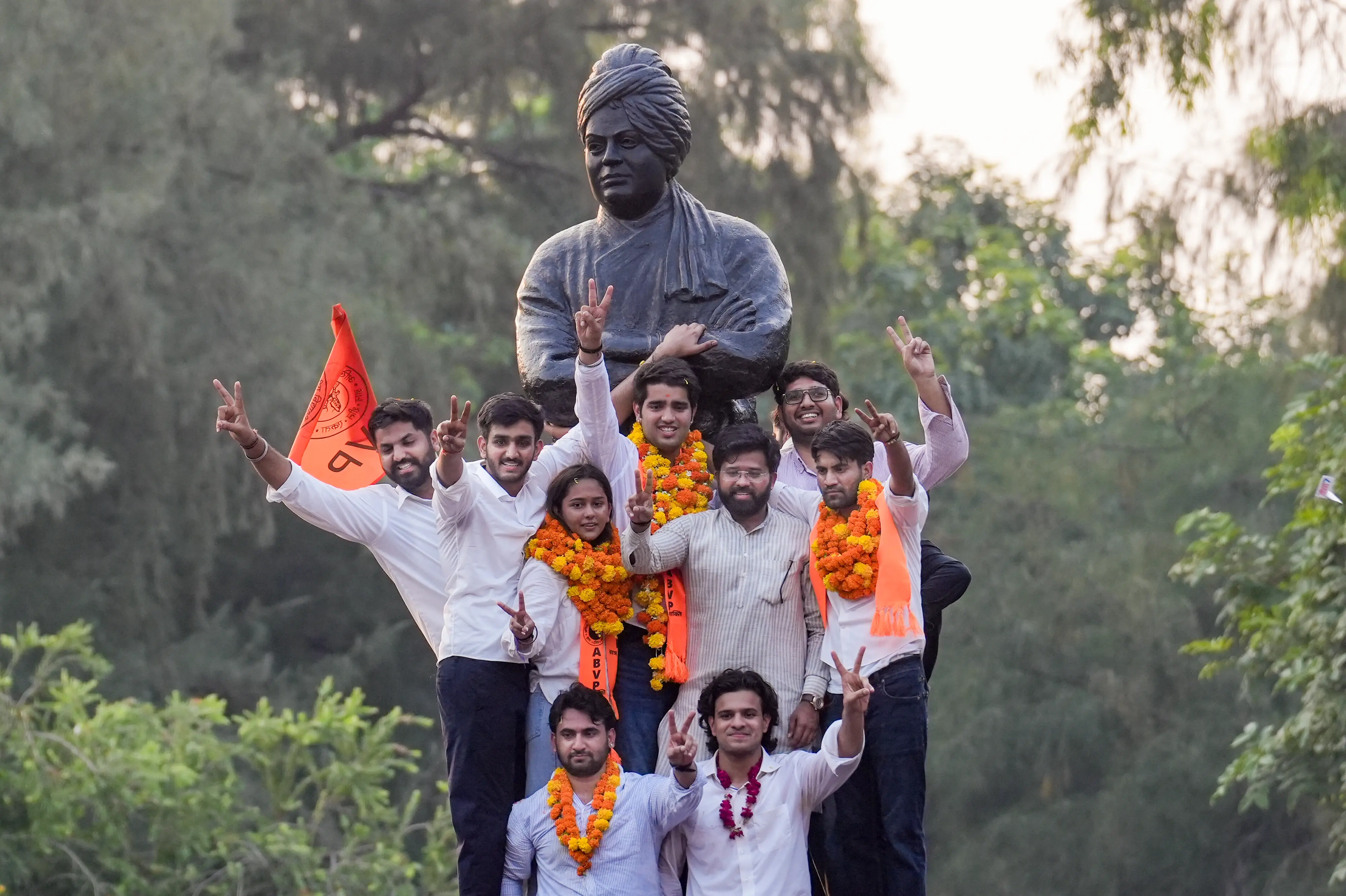 Akhil Bharatiya Vidyarthi Parishad's (ABVP) Yash Dabas, Riya Chhawdi and Lakshay Raj Singh celebrate with others as they climb atop Swami Vivekanand's statue after winning three of the four central panel posts in the Delhi University Students' Union (DUSU) elections, at the Faculty of Arts, in New Delhi.| Photo: PTI